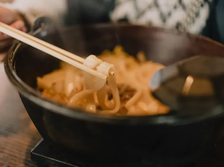 Chopsticks lifting noodles from a pan